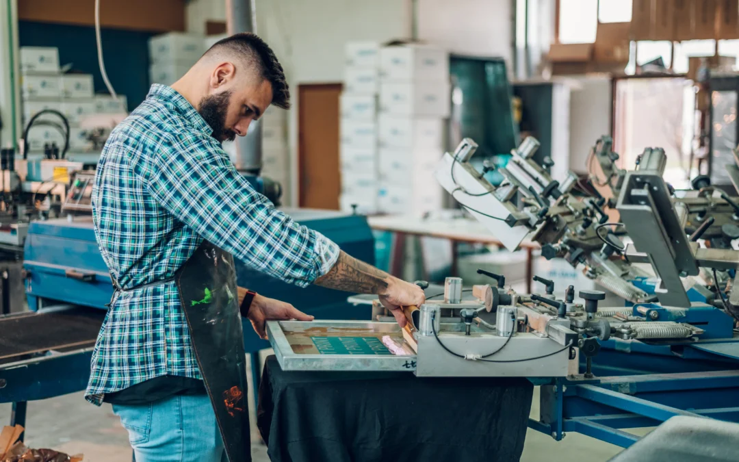 male worker pressing ink on frame while using the heat press machine to create a personalised t shirt